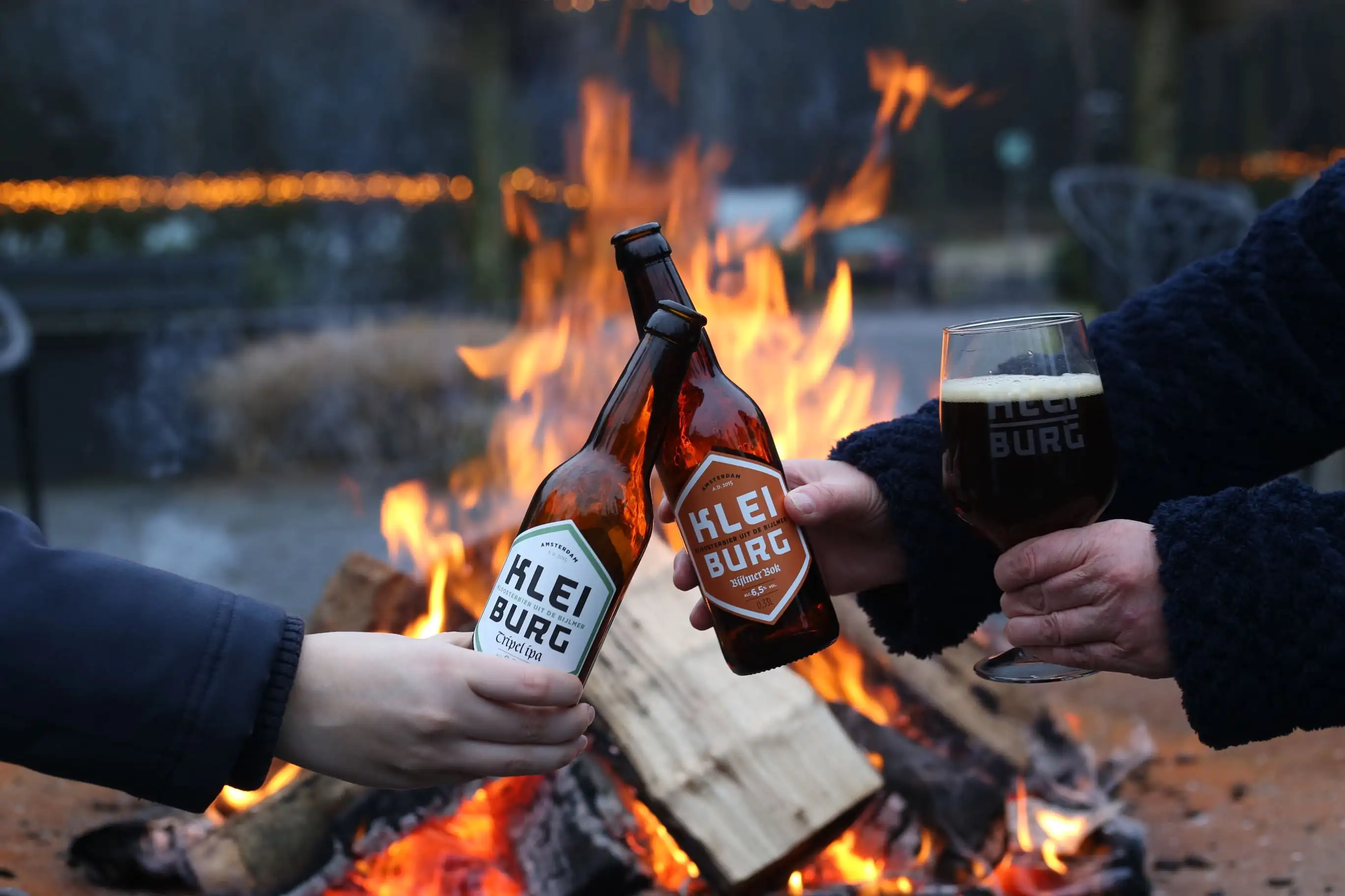 Twee flesjes kleiburg bier proosten voor een kampvuur